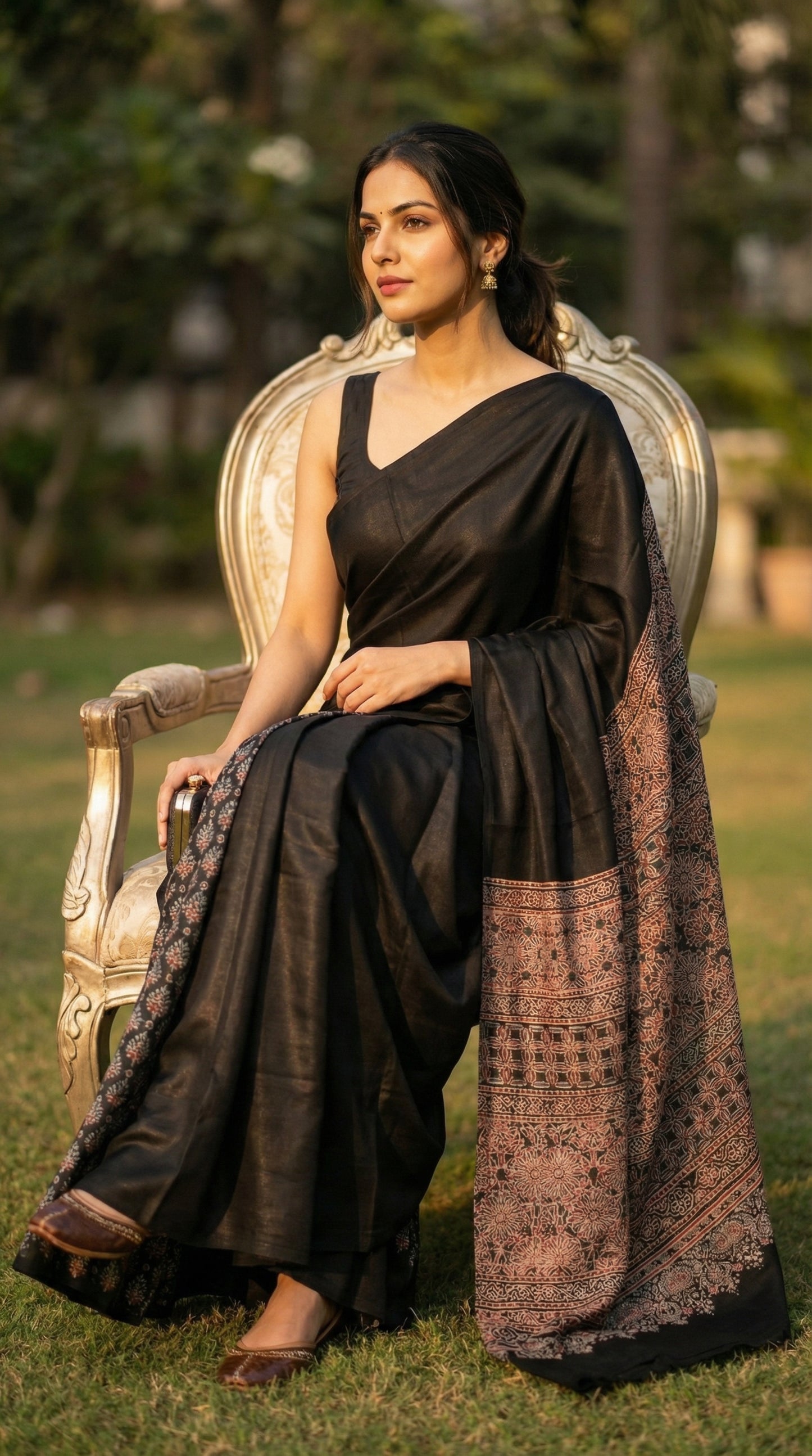 Woman in a black pure modal silk saree with intricate Ajrakh printed pallu, sitting outdoors on a chair.