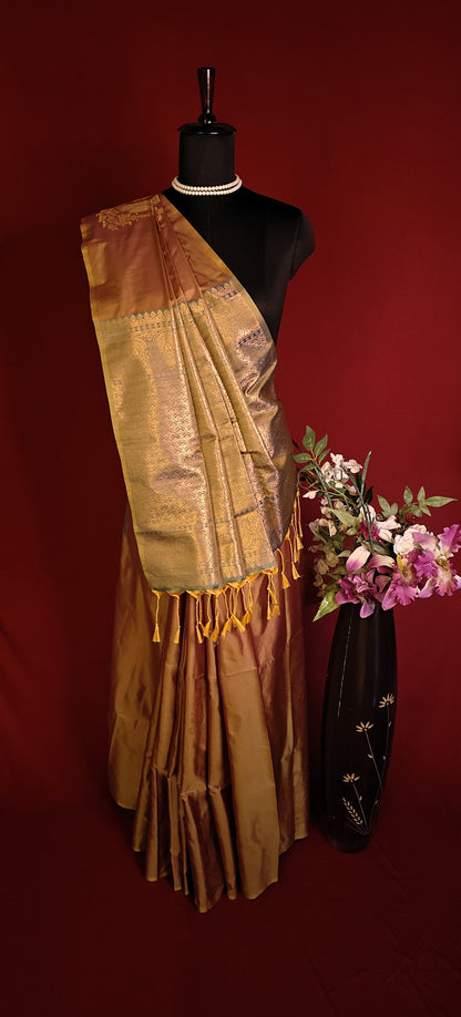Copper brown blended silk saree with golden zari border and scattered butis, styled on mannequin with a vase of flowers on a red background.