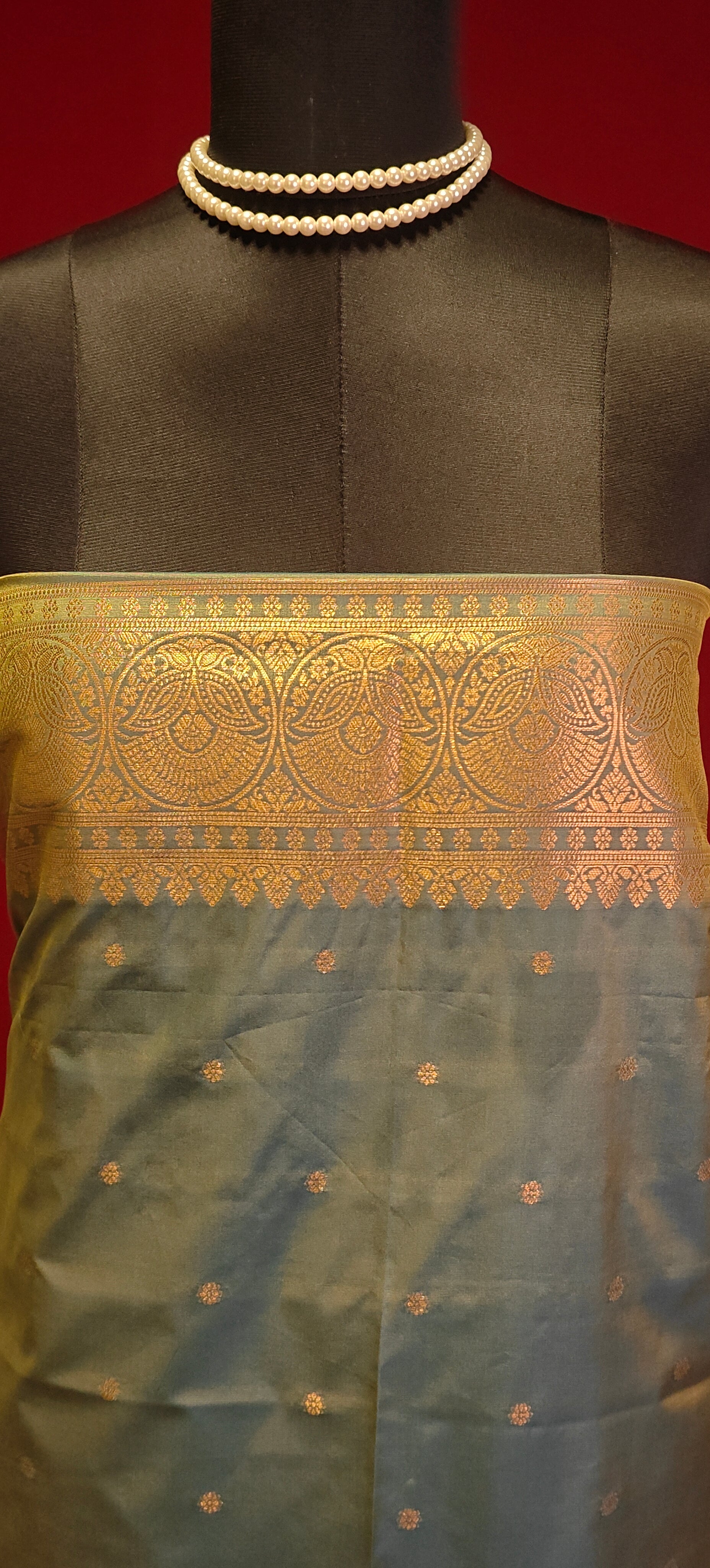 Copper brown blended silk saree with golden zari border and scattered butis, styled on mannequin showcasing it's blouse piece in blue against red background.