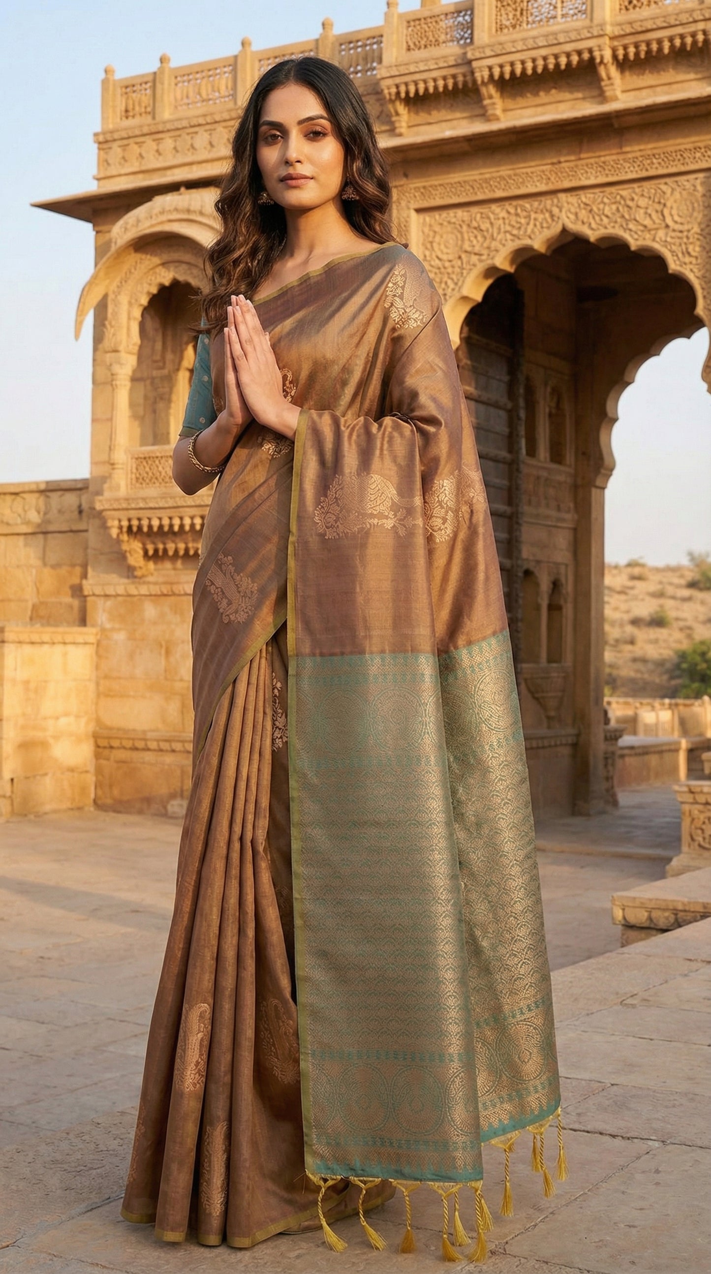 Woman in a copper brown blended silk saree with golden Zari border and scattered butis standing in front of an architectural structure.