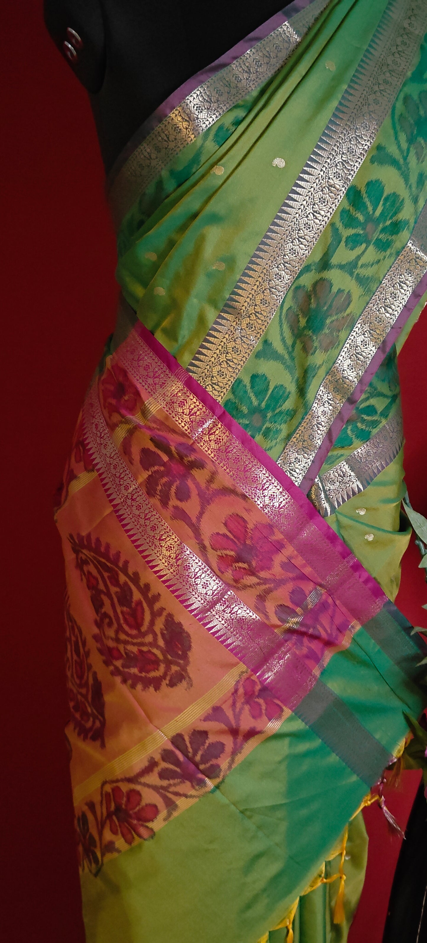 Green blended silk saree with elegant zari border and festive drape on a mannequin against red background.