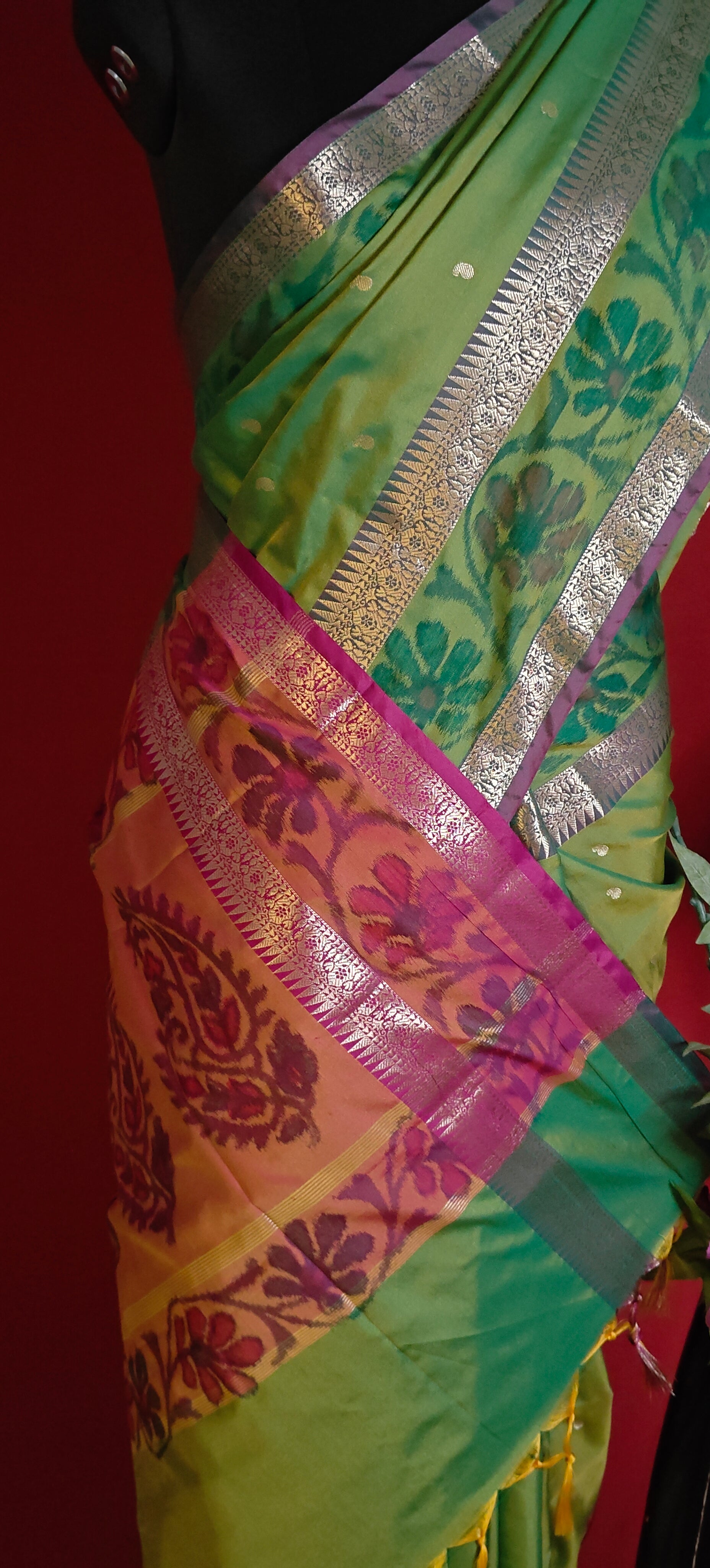 Green blended silk saree with elegant zari border and festive drape on a mannequin against red background.