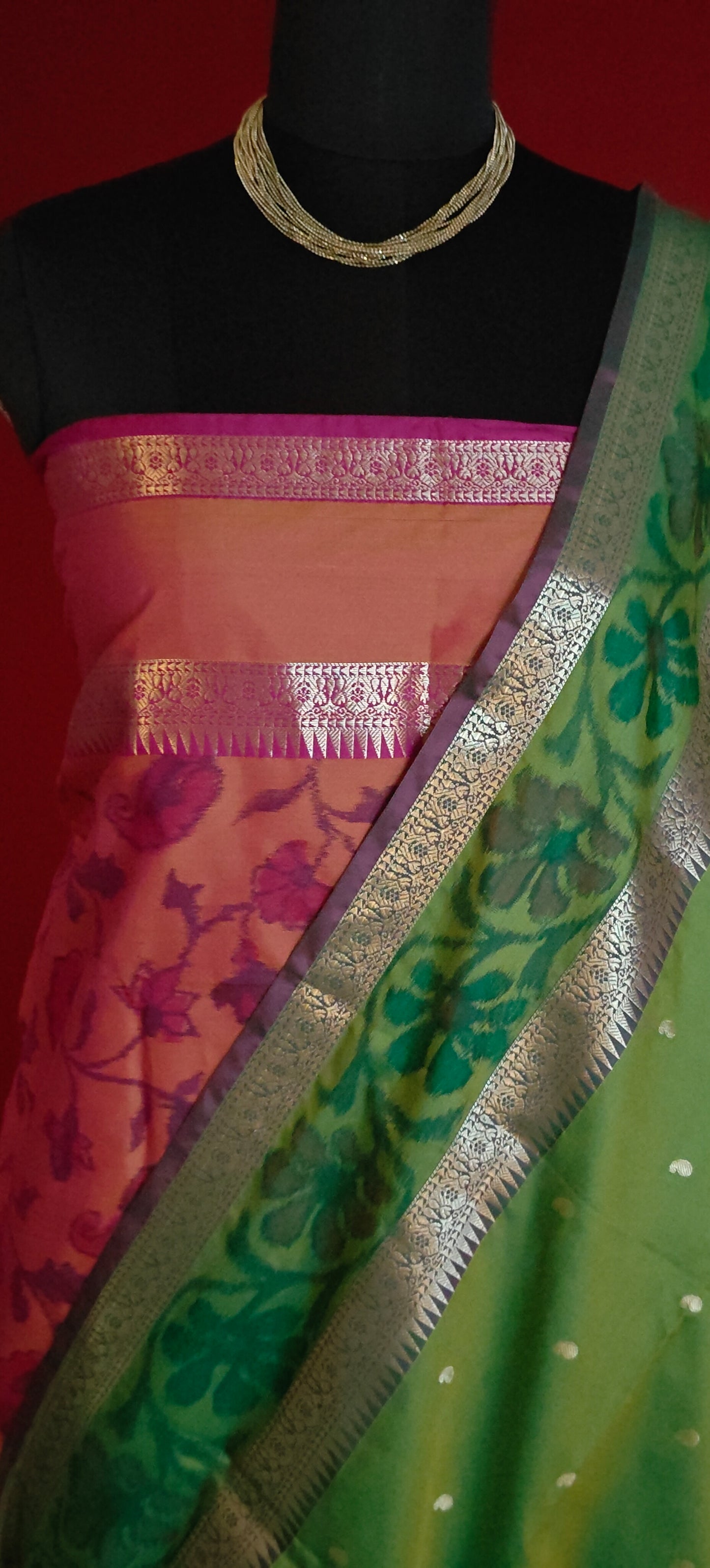 Green blended silk saree with elegant zari border and festive drape on a mannequin along with a flower vase against red background.