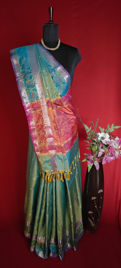 Green color blended silk saree with broad golden zari border and smooth finish on a mannequin with a vase of flowers against a red background
