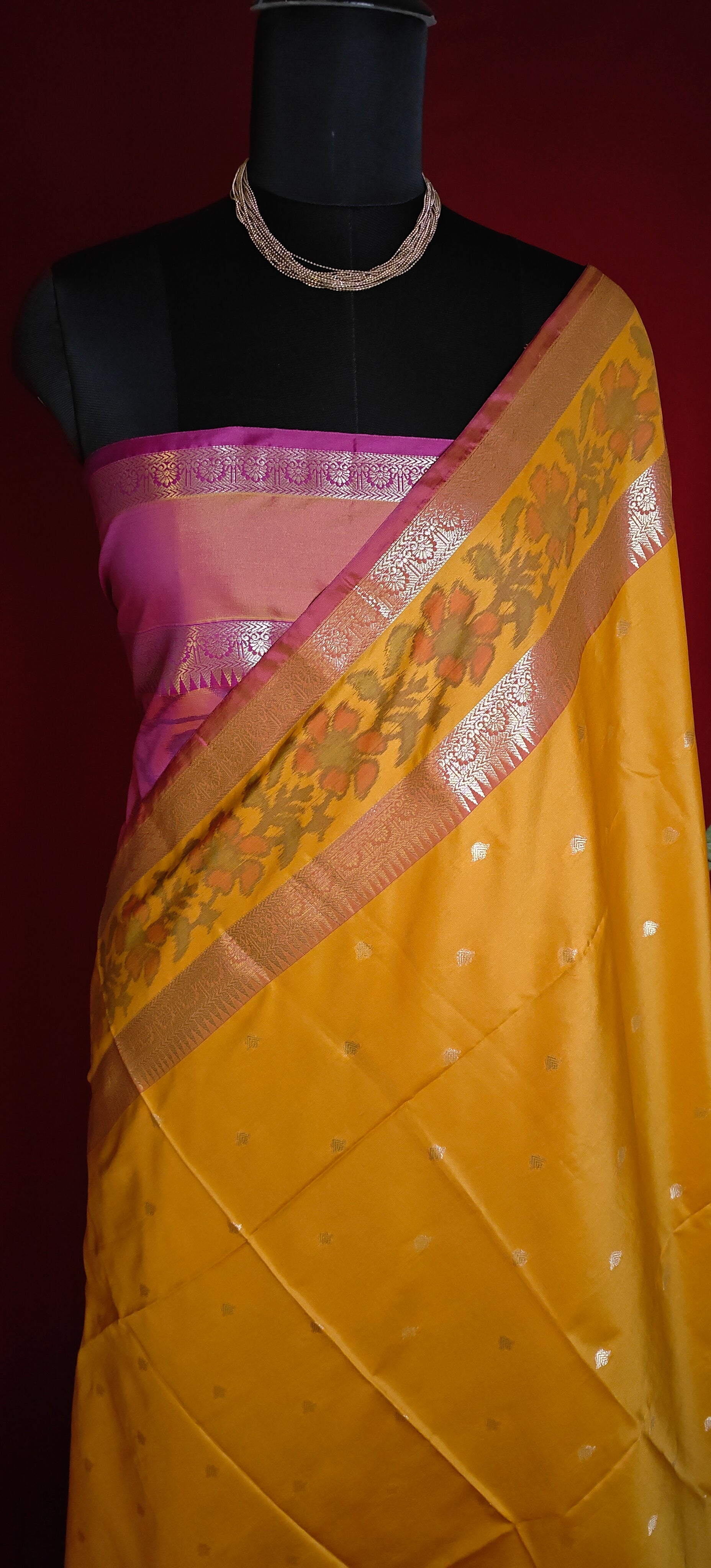Yellow blended silk saree with pink bloused and shimmering zari border, styled on mannequin against a dark background.