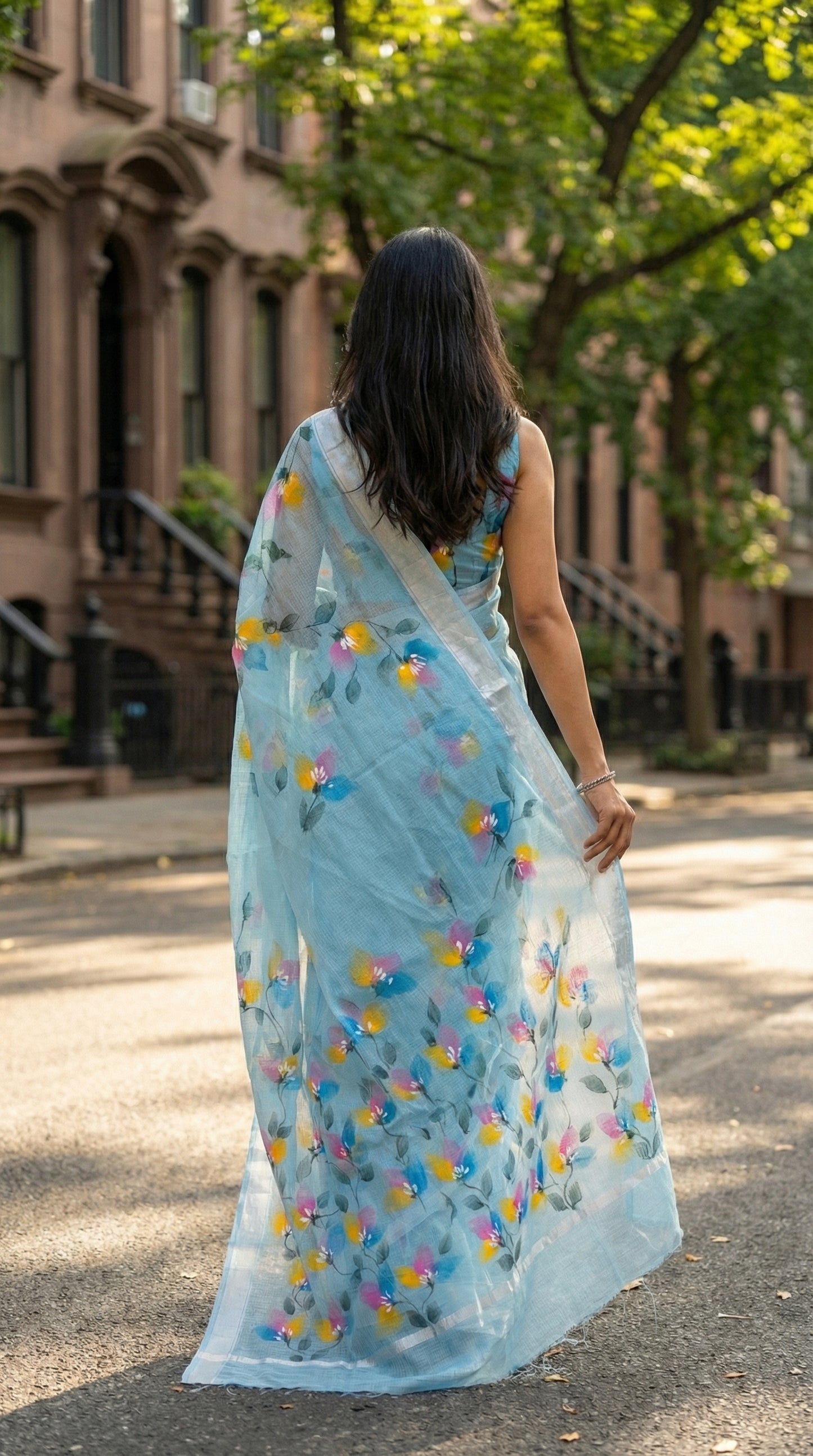 Woman in a blue-hand-painted-cotton-saree, walking on a street.