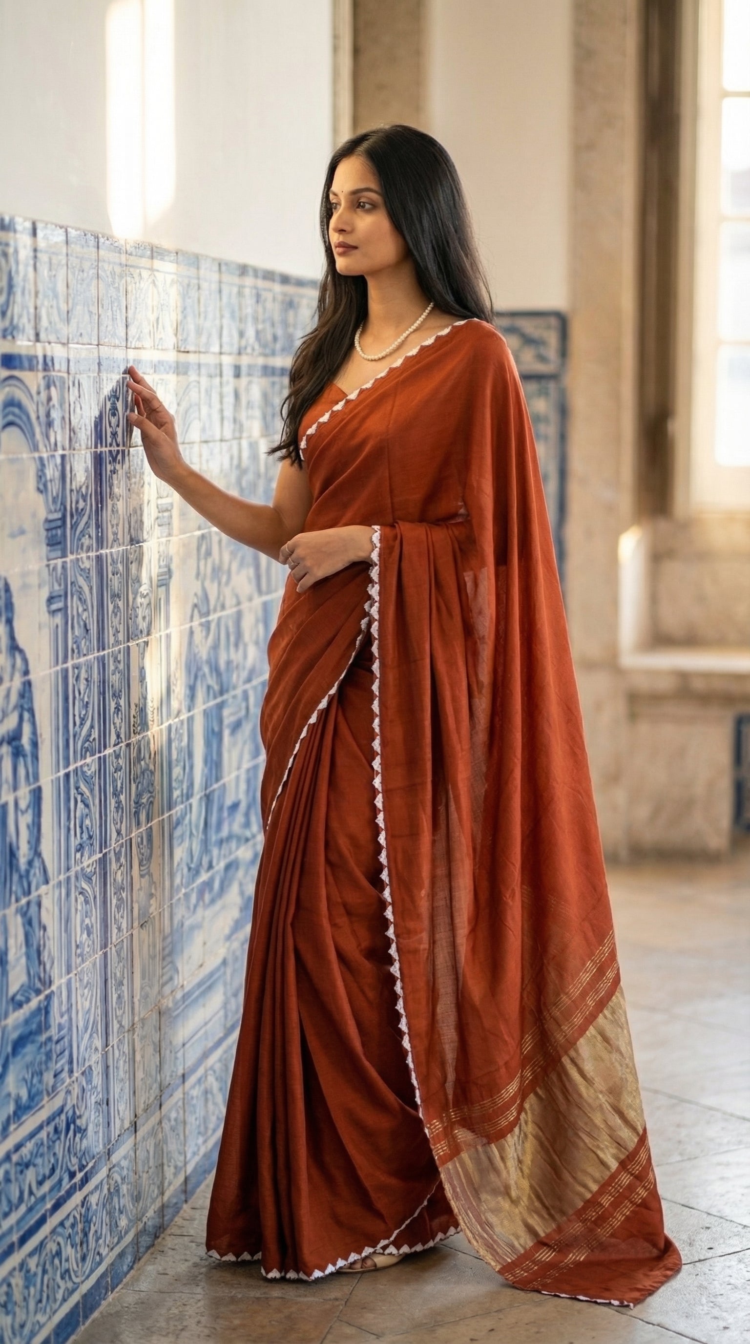 Woman in a burnt-orange-modal-silk-saree-lagdi-patta-pallu, standing next to an artistic wall.
