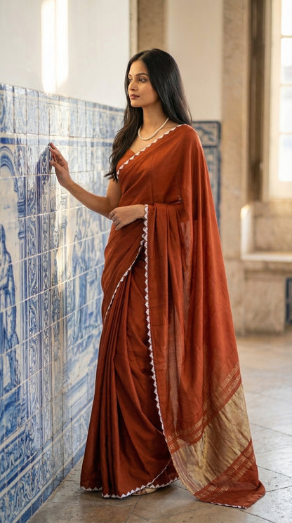 Woman in a burnt-orange-modal-silk-saree-lagdi-patta-pallu, standing next to an artistic wall.