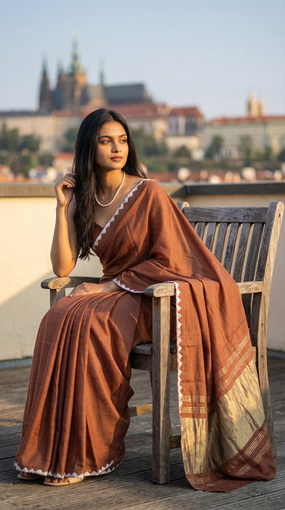 Woman wearing a chocolate-brown-modal-silk-saree-lagdi-patta-pallu, sitting in a chair on roof-top.