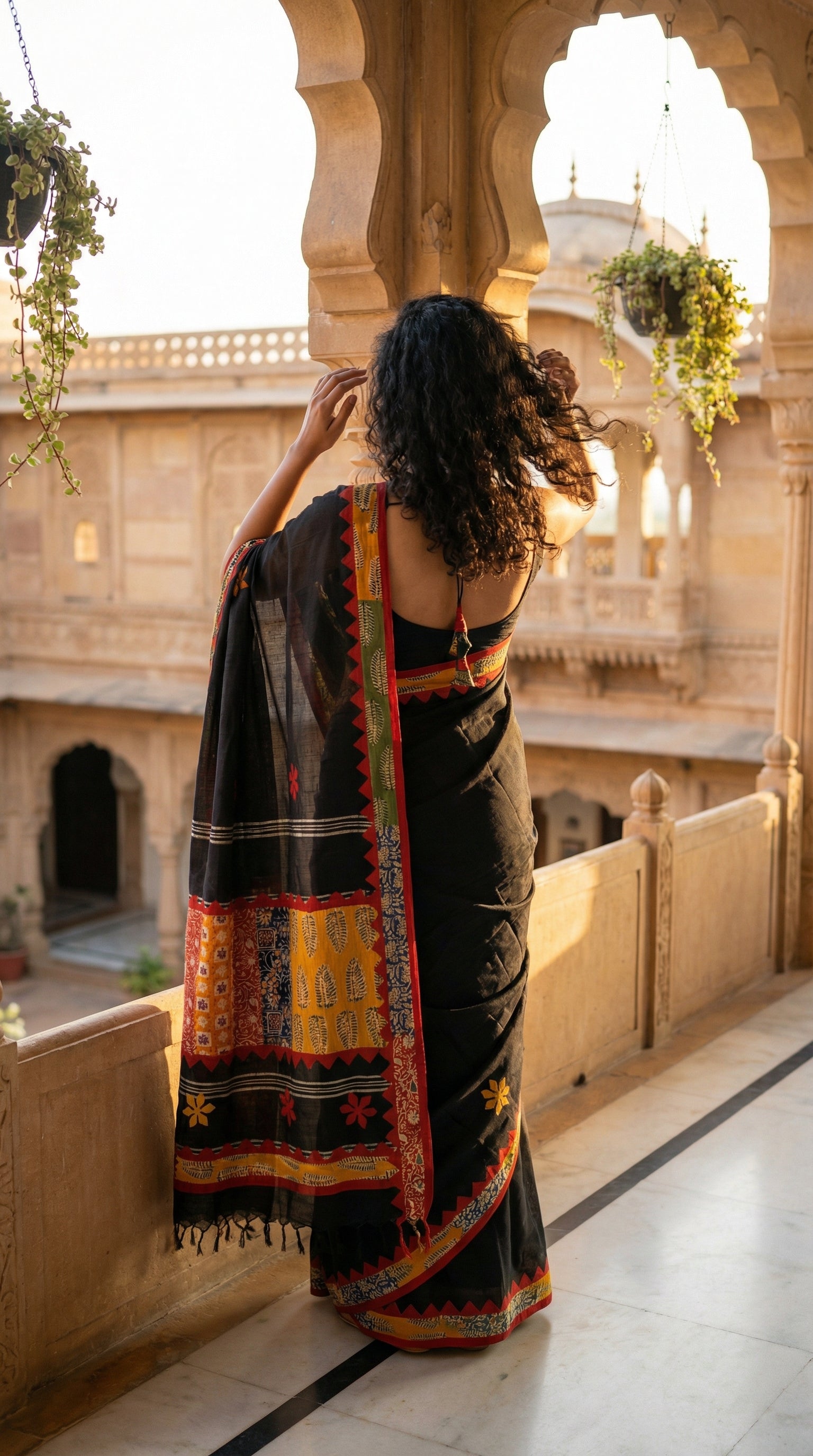 Woman in a black cotton saree with bold appliqué designs and traditional motifs, elegant ethnic wear for festive occasions standing on a balcony.