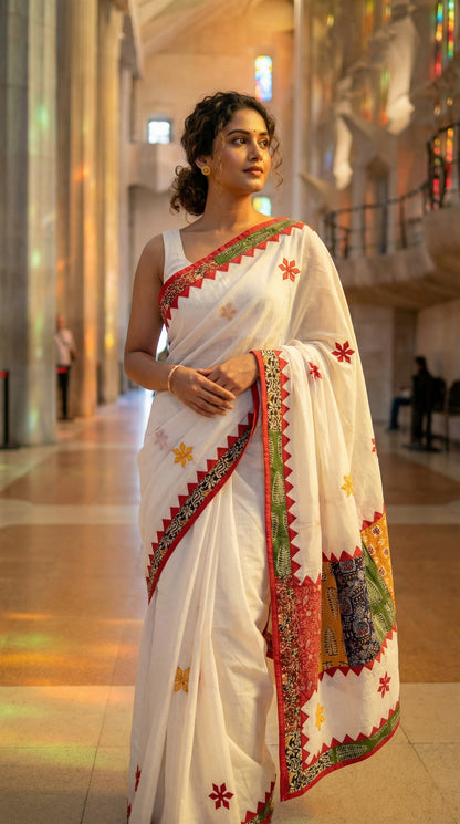 Woman wearing a white cotton saree with colorful appliqué patchwork and embroidered motifs, handcrafted traditional Indian attire in an indoor setting.