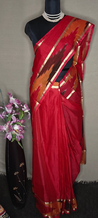 Magenta cotton saree with multicolor Ikat border and golden trim, folded with floral decor on a mannequin against a plain background.