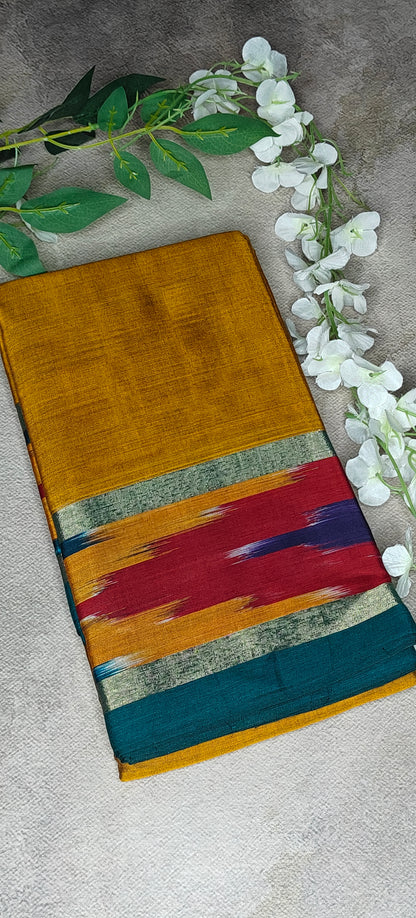 Mustard yellow cotton saree with abstract Ikat border in red, blue, and green, folded with floral decor with neutral background.