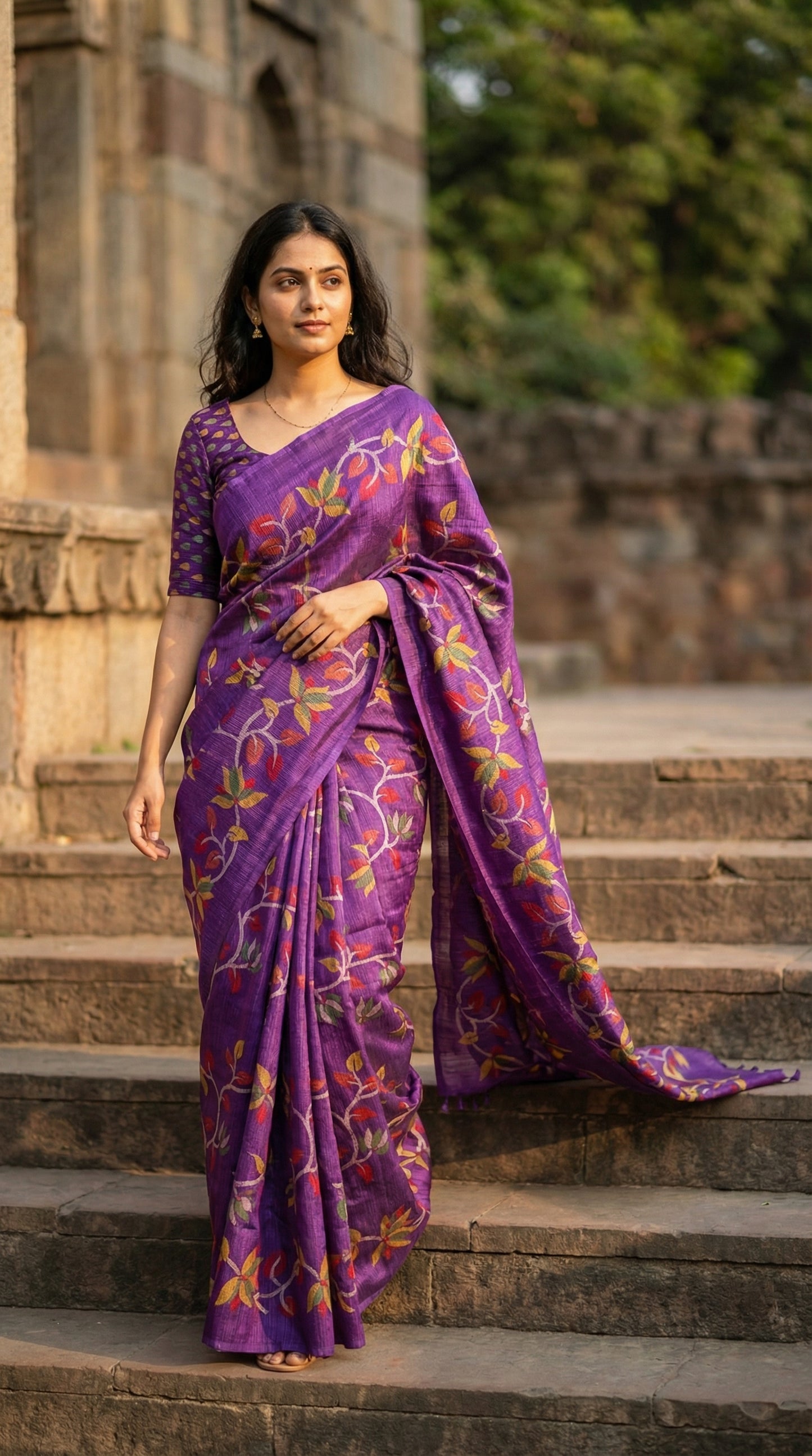 Woman wearing Designer Kota Blend Saree – Purple with Multicolor Leaf & Vine Motifs saree draped walking down steps in an architectural setup.