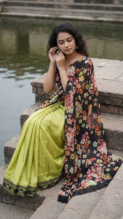 Woman in a designer silk saree with printed organza pallu – black & mint green floral elegance sitting by a body of water