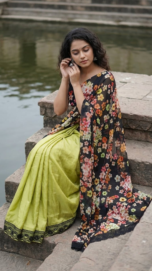 Woman in a designer silk saree with printed organza pallu – black & mint green floral elegance sitting by a body of water