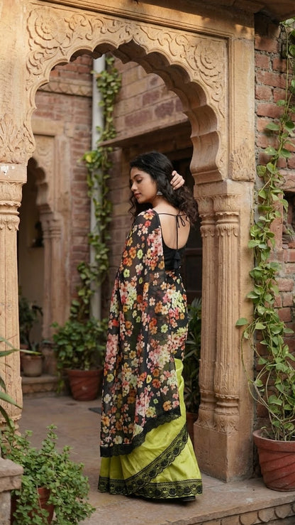Woman in a designer silk saree with printed organza pallu – black & mint green floral elegance standing in an architectural setting with plants.