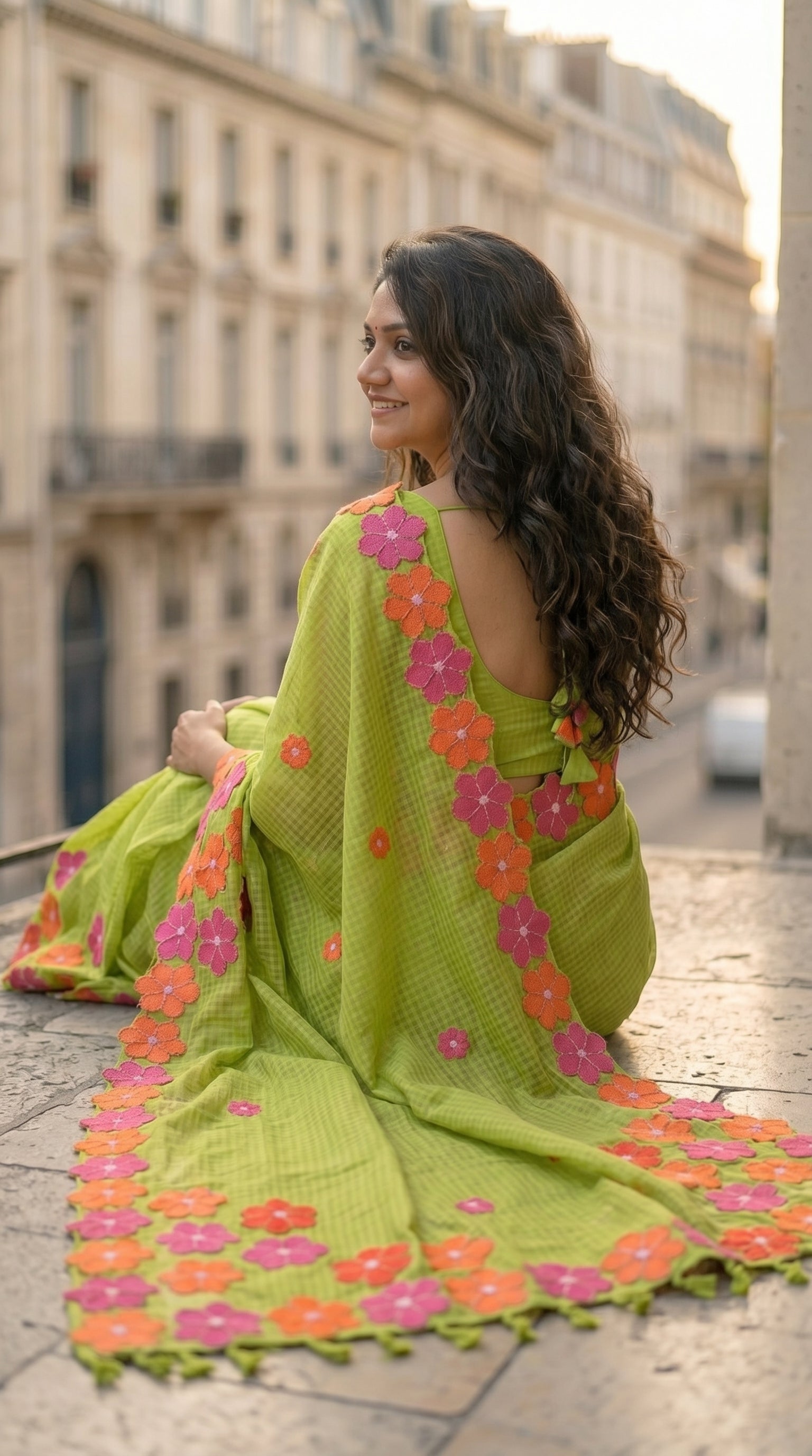 Woman in a green-mirror-work-kota-saree, sitting on a stone ledge in an urban setting.