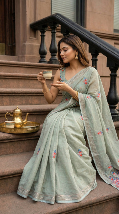 Woman wearing a grey-chanderi-kantha-saree, sitting on steps, holding a cup.