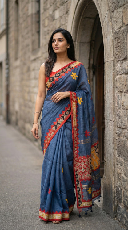 Woman in a grey linen cotton saree with traditional applique border, standing against a stone wall.