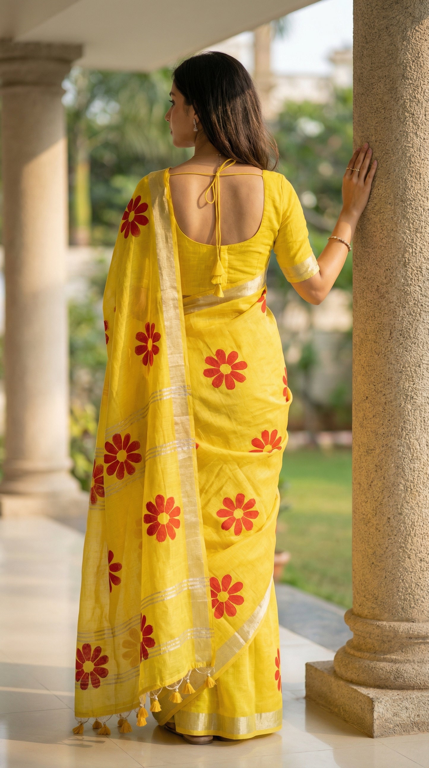 Woman wearing yellow cotton saree featuring hand-painted sunflower design with white and yellow petals, standing by a stone column.