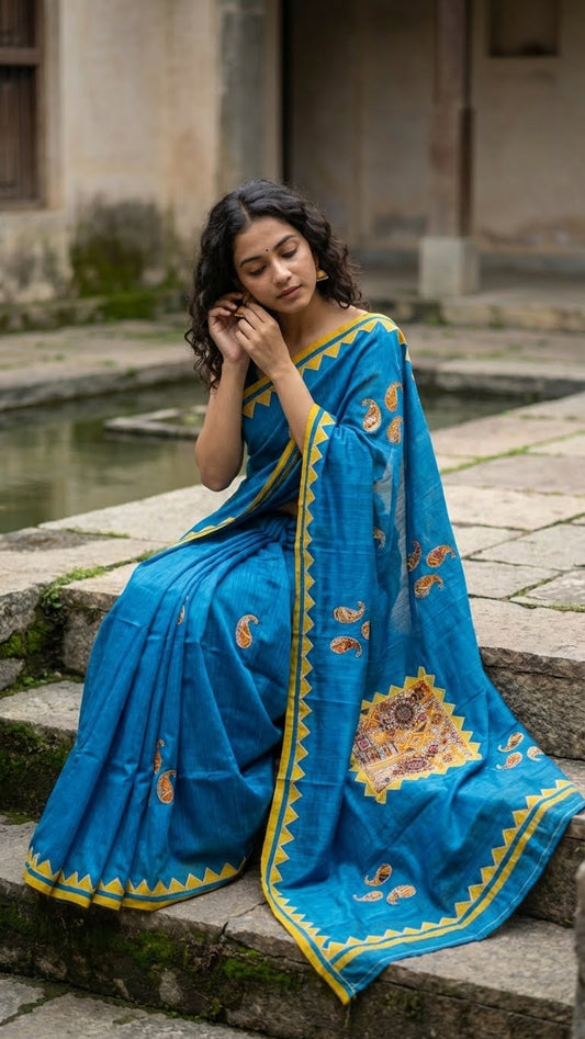 Woman in a handcrafted cotton appliqué saree – traditional motifs sitting on stone steps.