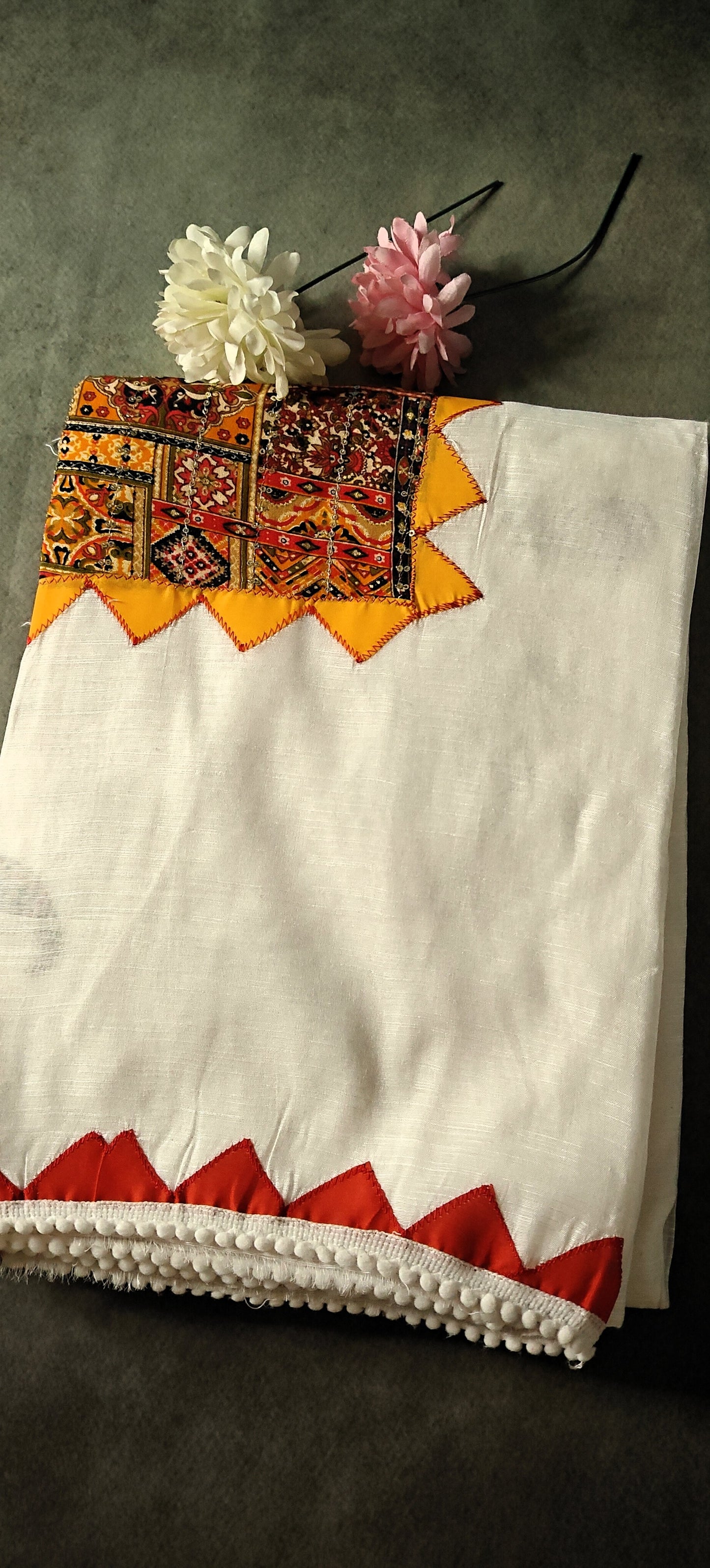 White cotton saree with colorful hand-appliqué embroidery and red-yellow geometric border.