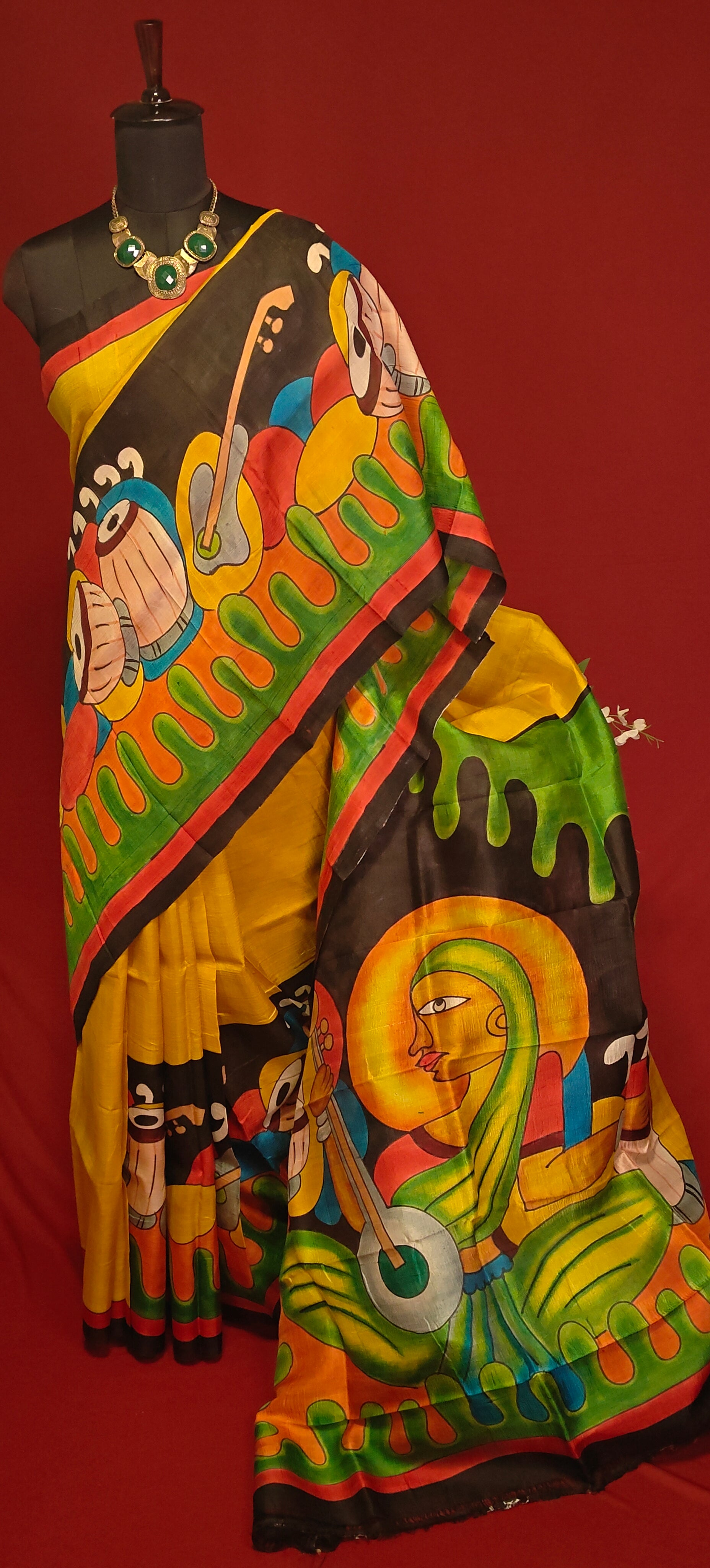 Hand-painted pure silk saree in dual-tone yellow and black with artisan detailing and luxurious drape on a mannequin against a red background.