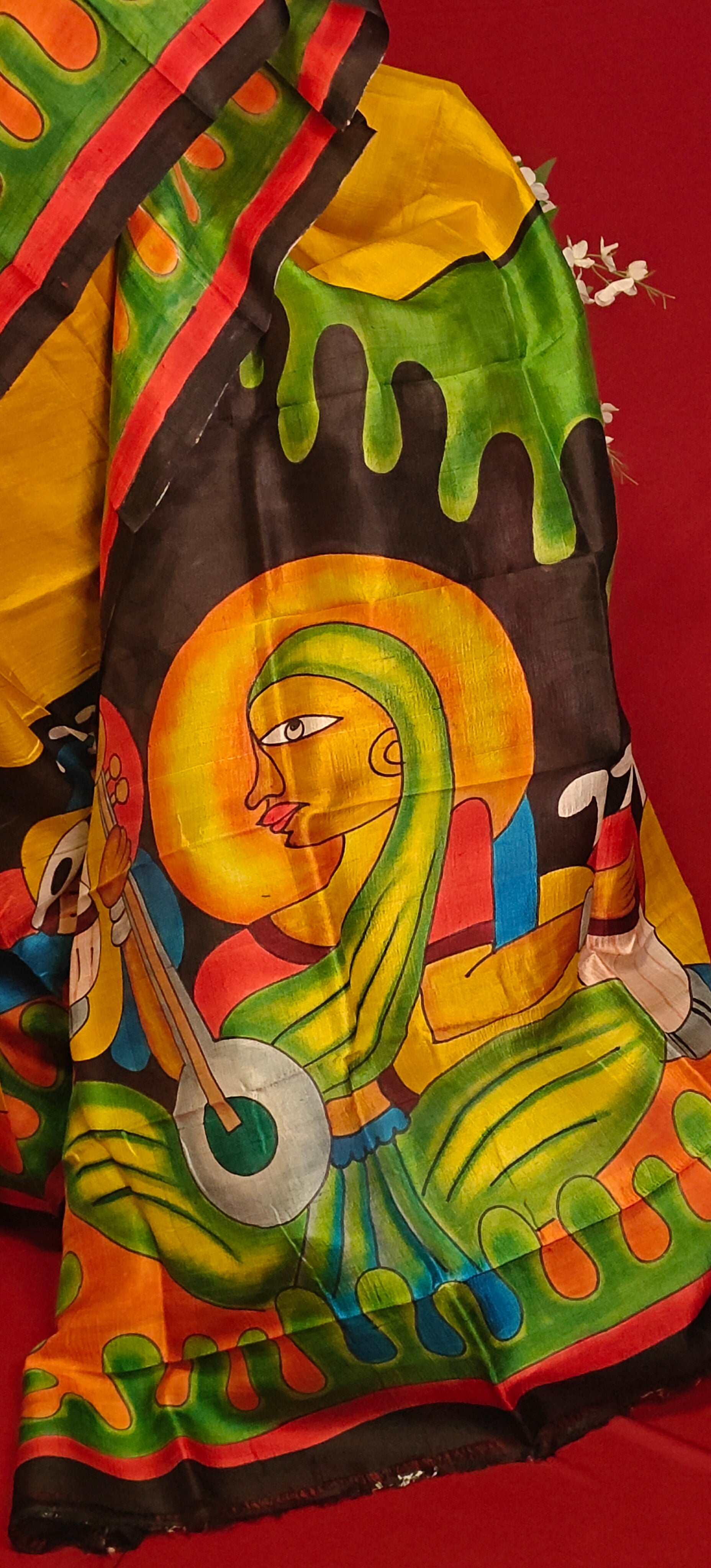 Hand-painted pure silk saree in dual-tone yellow and black with artisan detailing and luxurious drape in it's pallu against red background.