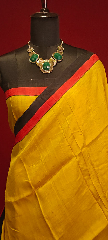 Hand-painted pure silk saree in dual-tone yellow and black with artisan detailing and luxurious drape showcasing the blouse piece on a mannequin against a red background.