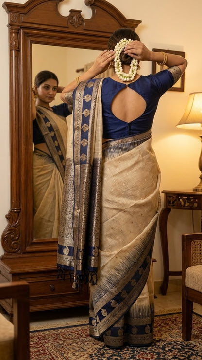 A lady wearing Beige Hasthkala blended silk saree featuring a royal blue gold zari border and temple motifs looking at the mirror in her house and adjusting her hairs.