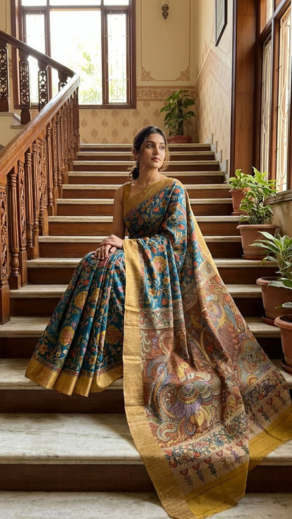 Woman in a blue saree with kalamkari-inspired floral vine digital print and golden border standing on a staircase with decorative elements.