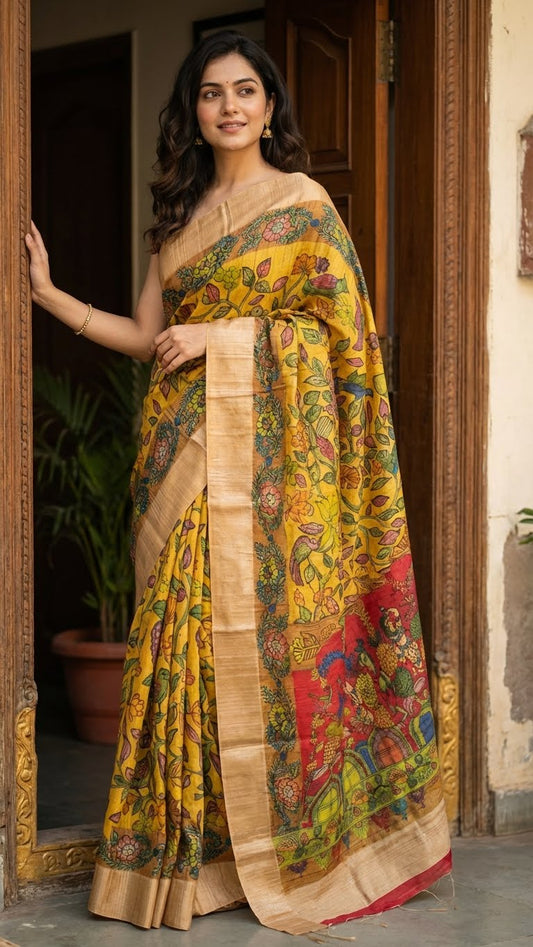 Woman wearing a yellow saree with kalamkari-style bird and floral digital print and golden border, standing in a doorway.