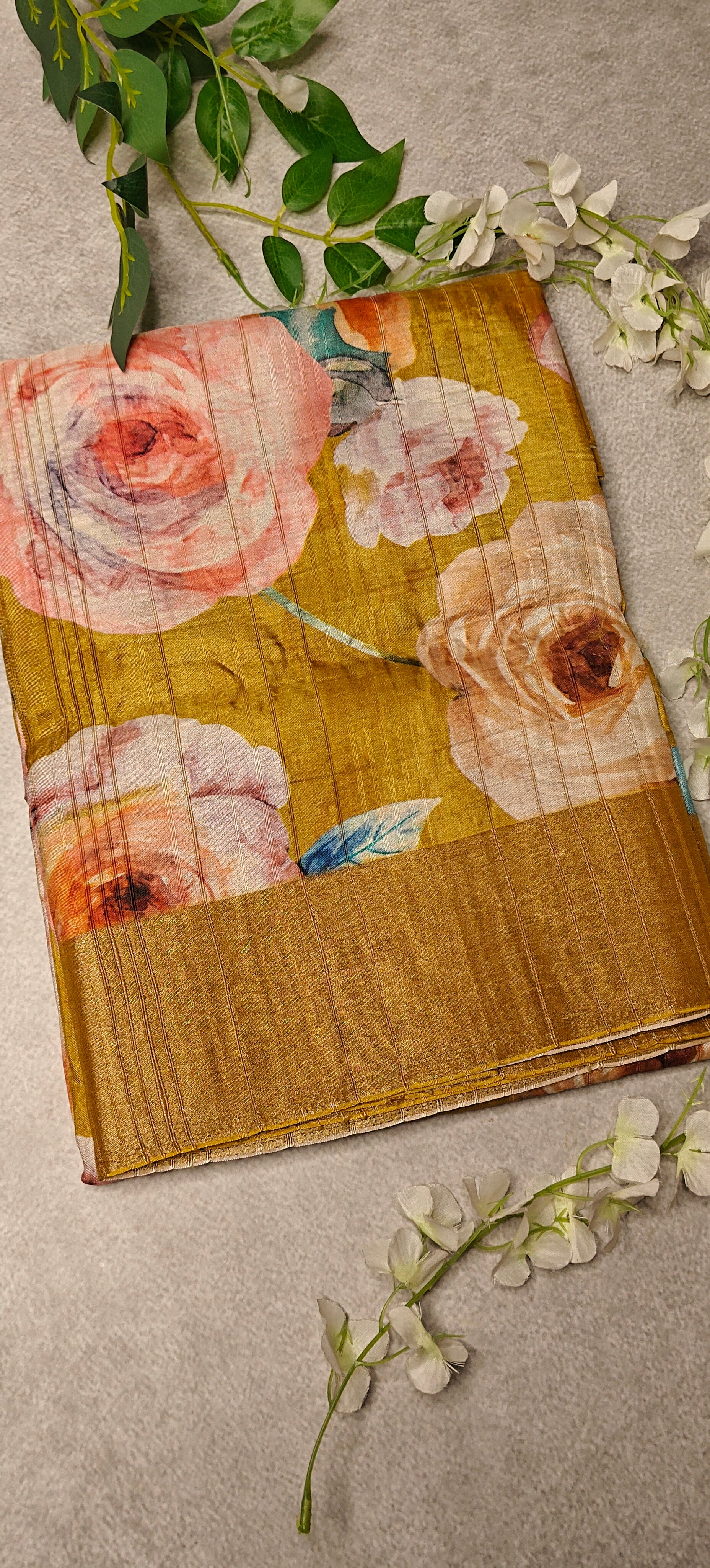 Golden yellow blended silk saree with Kalamkari-inspired floral digital print in pink, blue, and purple tones on a textured surface with greenery.