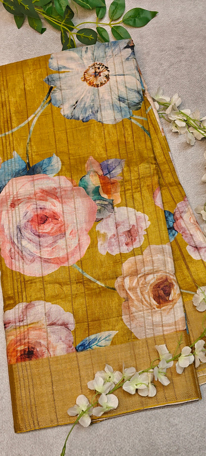 Golden yellow blended silk saree with Kalamkari-inspired floral digital print in pink, blue, and purple tones on a textured surface with greenery.