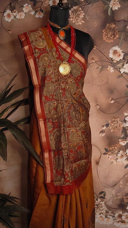 Maroon blended silk saree with Kalamkari-inspired floral and paisley digital print and broad golden border on a mannequin against a floral background.
