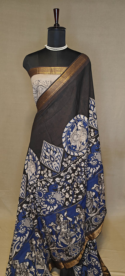 Black silk saree with Kalamkari-style floral and paisley print and golden border on a mannequin wearing a pearl necklace, against a plain background.