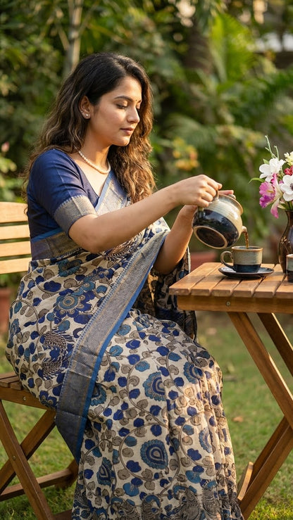 Woman in a indigo silk saree with kalamkari-inspired digital print and golden border pouring tea outdoors.