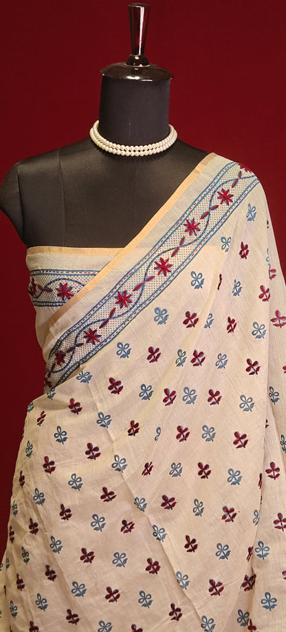 Handcrafted Kantha stitched silk blend saree in cream with multicolor floral and bird embroidery in blue tones on a mannequin showcasing blouse piece against a red background.