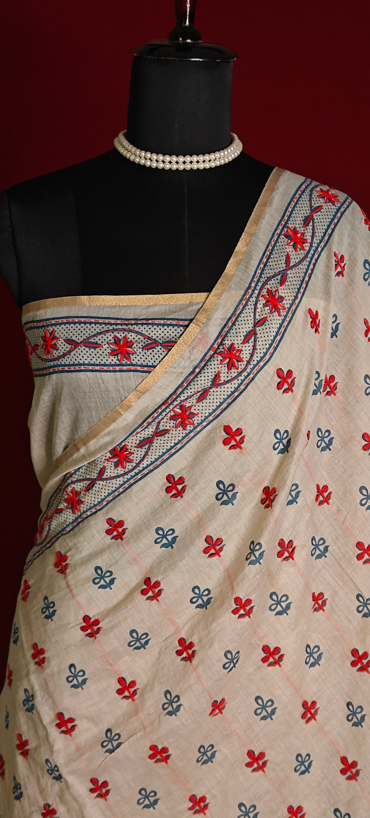 Handcrafted Kantha stitched silk blend saree in cream with multicolor floral and bird embroidery on a mannequin showcasing the blouse piece against a red background.