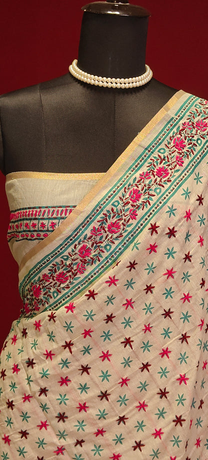 Handcrafted Kantha stitched silk blend saree in cream with pink and sea green floral embroidery on a mannequin showcasing the blouse piece against a red background.