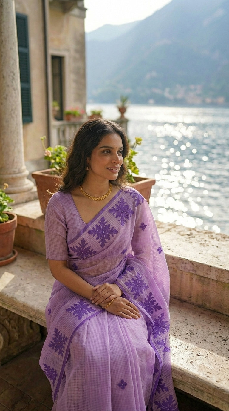 Woman in a lavender-purple-applique-kota-saree, sitting by a scenic lakeside.