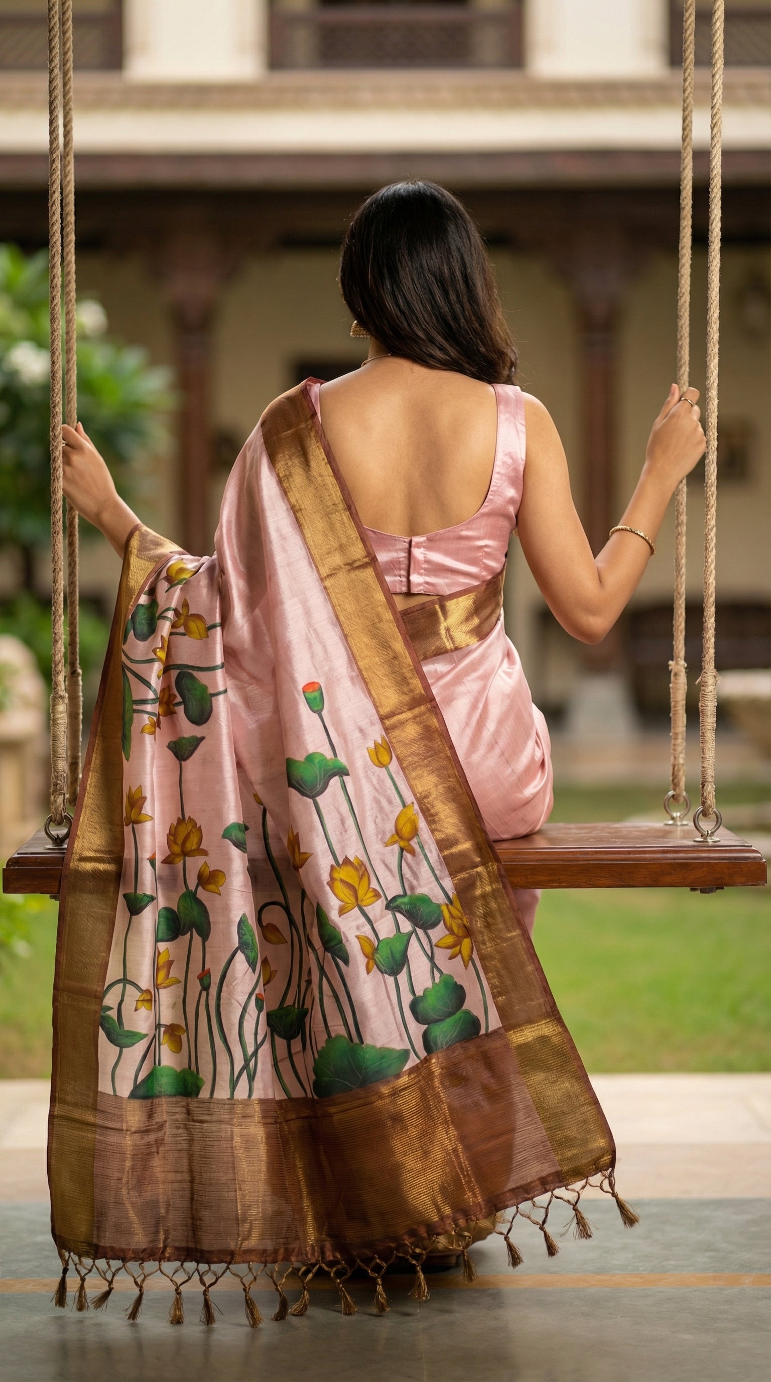 Woman in a traditional light-pink-viscose-silk-lotus-saree, sitting on a swing outdoors.