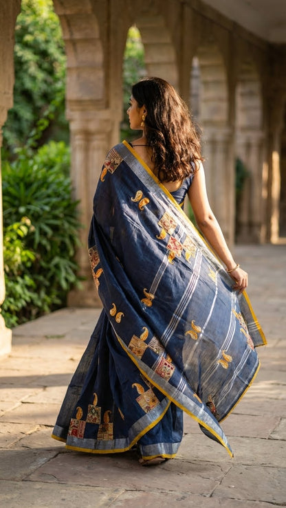 Woman in a grey linen cotton saree with applique work paisley motifs and silver thread detailing walking outdoors.