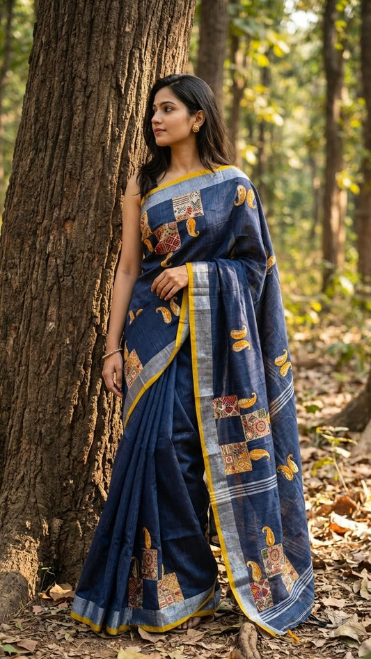 Woman in a grey linen cotton saree with hand-embroidered paisley motifs and silver thread detailing standing in a forest.