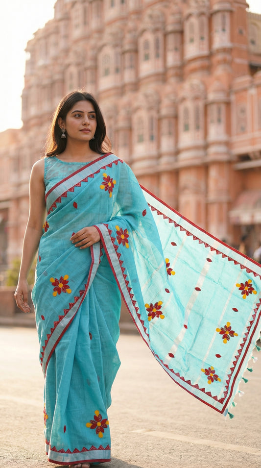 Woman in a sky blue linen cotton saree featuring vibrant appliqué floral motifs and applique work, lightweight festive attire, standing in front of Jaipur palace.