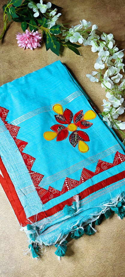Sky blue linen cotton saree featuring vibrant appliqué floral motifs and handcrafted embroidery, lightweight festive attire.