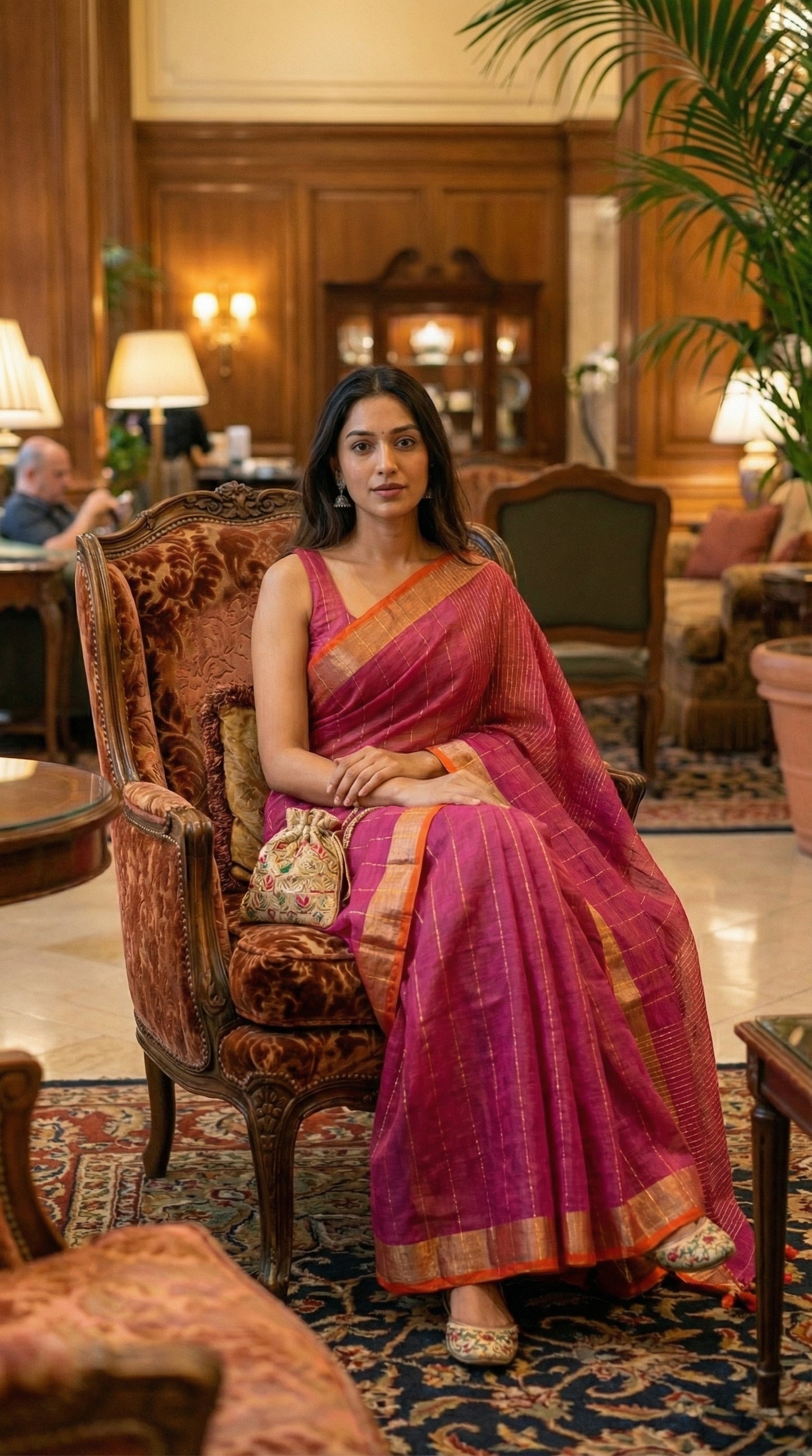 Woman in a magenta-cotton-linen-saree-Zari, sitting on an ornate chair in a luxurious room.