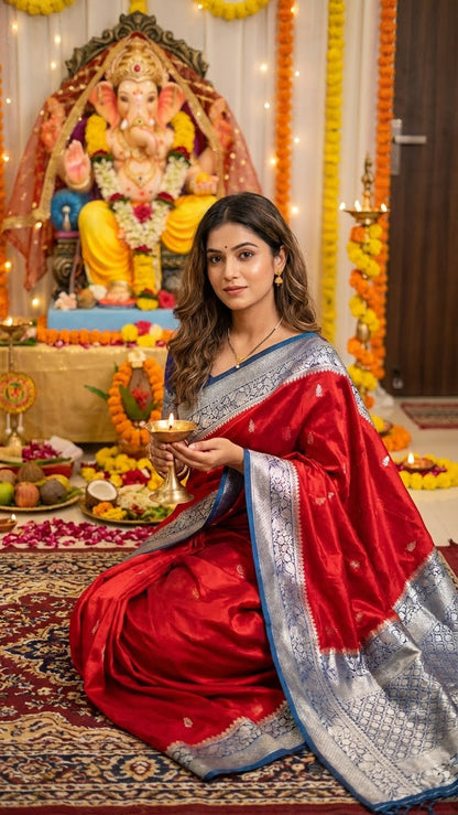 Woman in a Magenta Mashru silk saree with silver-blue ornate border sitting in front of a decorated altar with a deity statue.