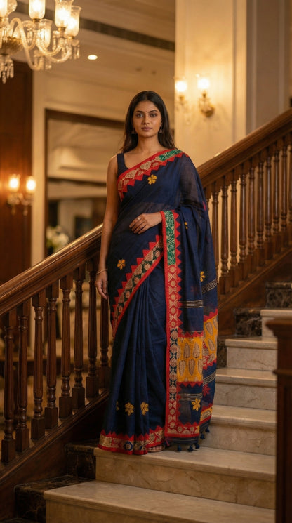 Woman in a midnight indigo linen cotton saree with handcrafted applique border, standing on a staircase in an elegant interior setting.